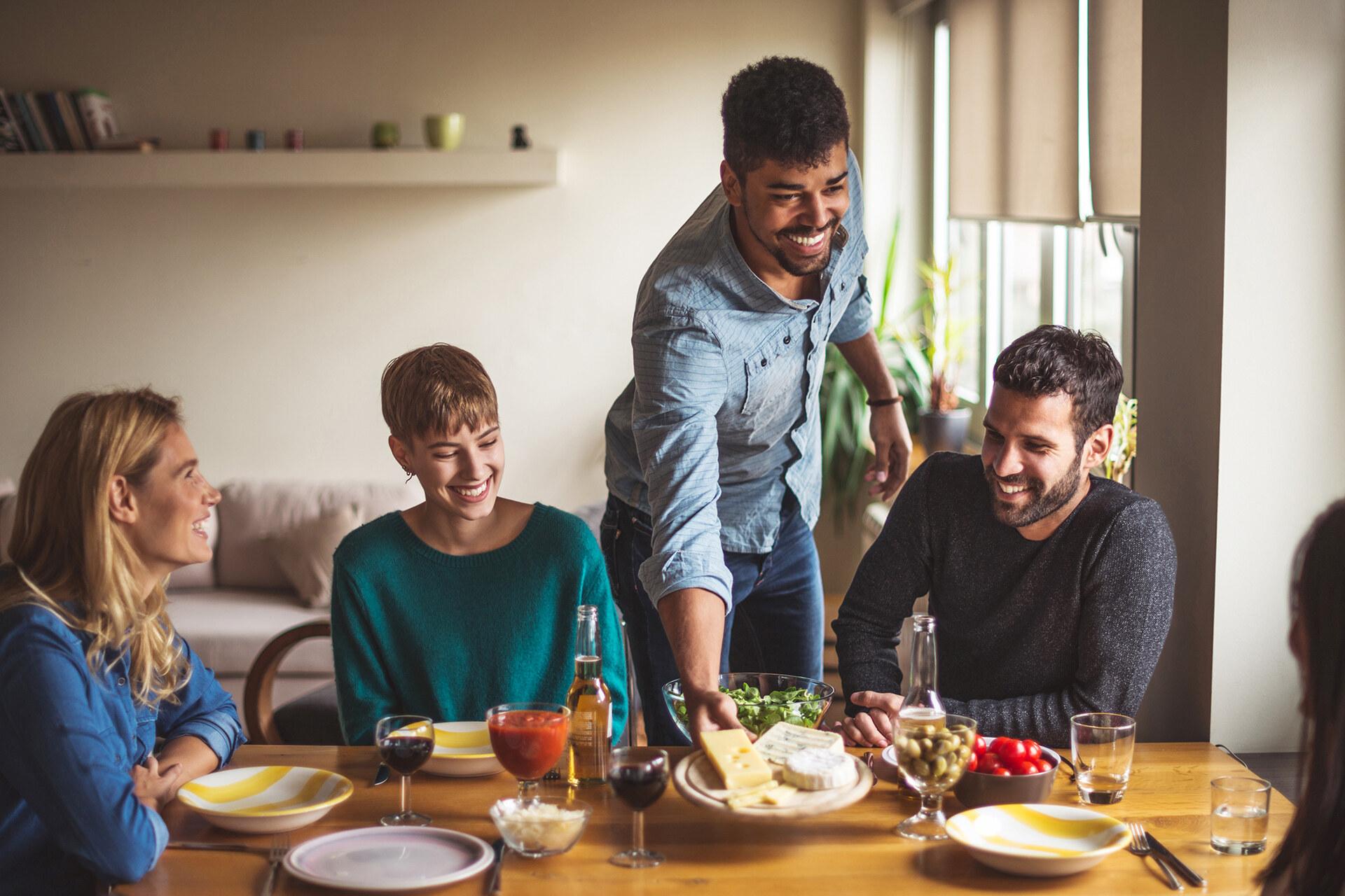 A group of smiling 30-somethings around a dinner table in a bright modern apartment