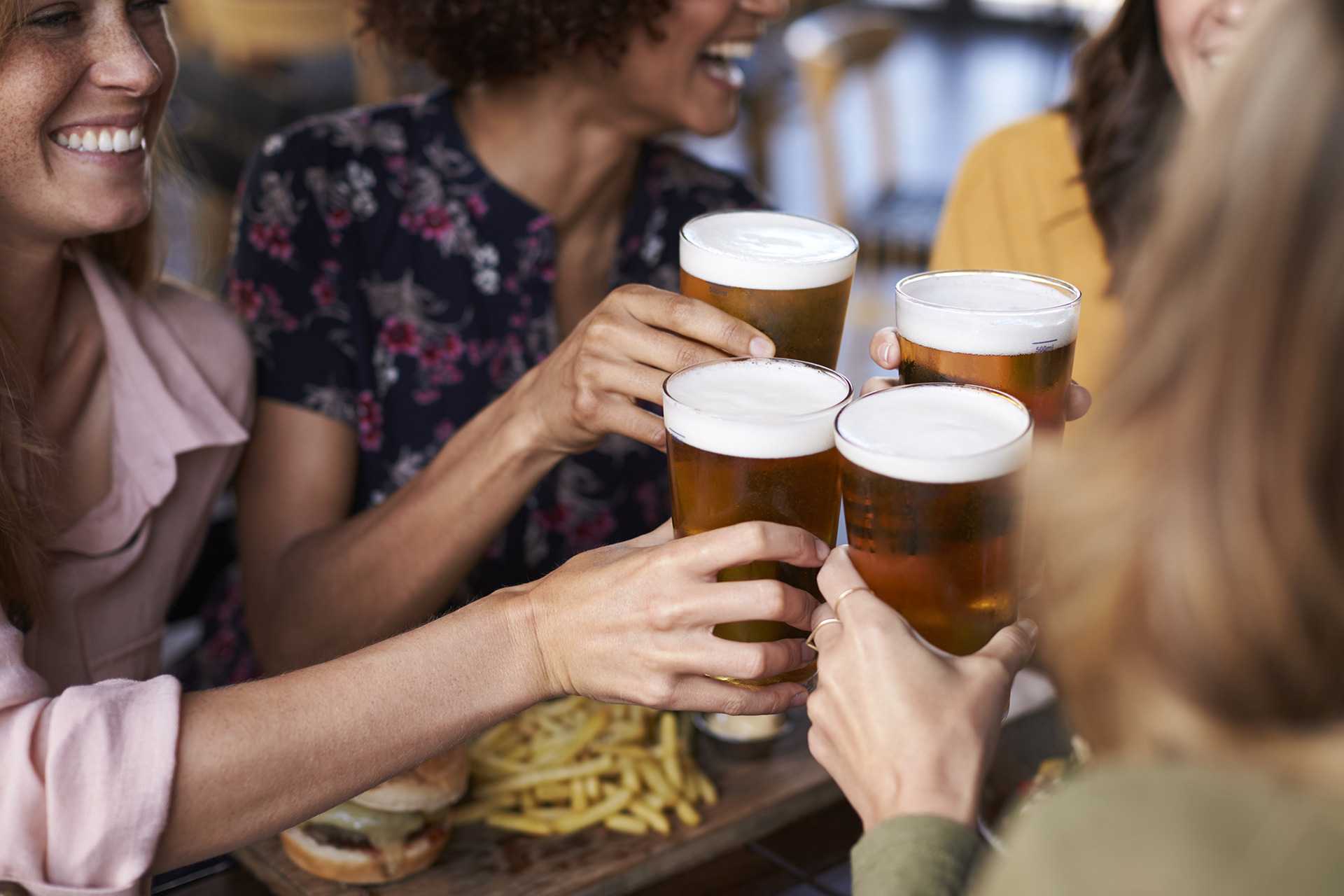 A close-up on the hands of a diverse group of women toasting with foam-topped beers