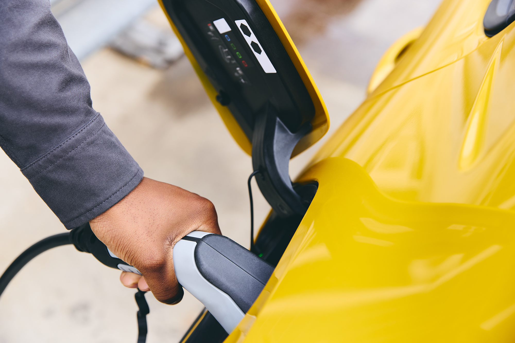 A man's hand inserting the nozzle of an electric vehicle charger into a yellow car